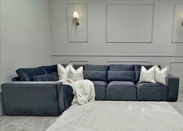 Gray sectional sofa with white pillows in a room with gray walls and a light gray rug.