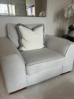 Gray armchair with a white pillow and decorative trim in a room setting.