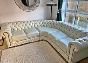 White tufted sectional sofa in a living room with a large window and decorative mirror.