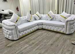 White sectional sofa with gold accents in a room with curtains and a fire extinguisher.