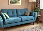 Blue sofa in a living room with a lamp, plant, and artwork on the wall.