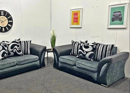 Two gray sofas with black and white patterned cushions in a room with framed pictures on the wall.