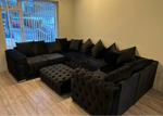 Black sectional sofa with tufted ottoman in a room with a window.