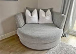 Gray swivel chair with decorative pillows in a room with light wood flooring and a window.