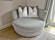 Gray swivel chair with decorative pillows in a room with light wood flooring and a window.